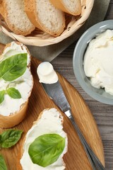 Delicious sandwiches with cream cheese and basil leaves on wooden table, flat lay