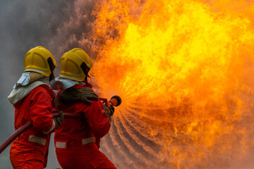 Firefighters teamwork in fire suit on rescue duty using water from hose extinguishing fighting with...