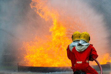 Obraz premium Firefighters teamwork in fire suit on rescue duty using water from hose extinguishing fighting with big crackle fire flames inside burning premises. Fireman spraying high pressure water fight a fire.