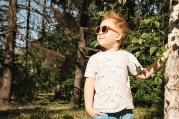 Portrait of a happy child in sunglasses against a background of green trees. Close-up. Happy boy with glasses enjoying the sun. Vacation, summer vacation concept. High quality photo