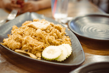 Green chicken curry fried rice dish with blurry customer hands background, nuts, cucumber slices served on wooden bowl at upscale Thai restaurant in Austin, Texas, Asian food lunch dinner dish