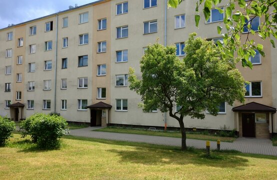 Four-story low building. A restored 1970s block of flats in a sunlit estate, next to a grassy field with recently mown grass.