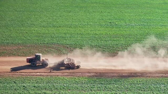 Tractor with small grader at speed along a dirt road and bringing up plenty of dust