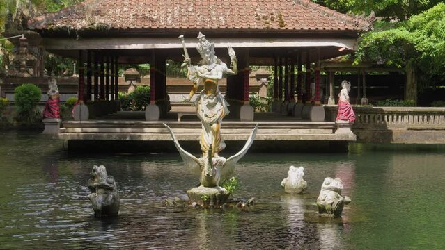 Serene view of the Pura Gunung Kawi Sebatu temple in Bali, Indonesia. A beautiful statue rises from the tranquil pond, surrounded by traditional architecture, evoking a sense of peace and spirituality
