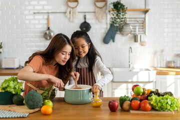Portrait of enjoy happy love asian family mother with little asian girl daughter child help cooking food healthy eat with fresh vegetable testing smell soup in a pot with spoon.helping mom in kitchen