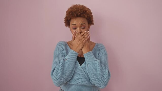 Shocked african american woman covering mouth with hands over mistake, secret under wraps. portrait of attractive lady in sweater, standing against pink background in stunned silence.