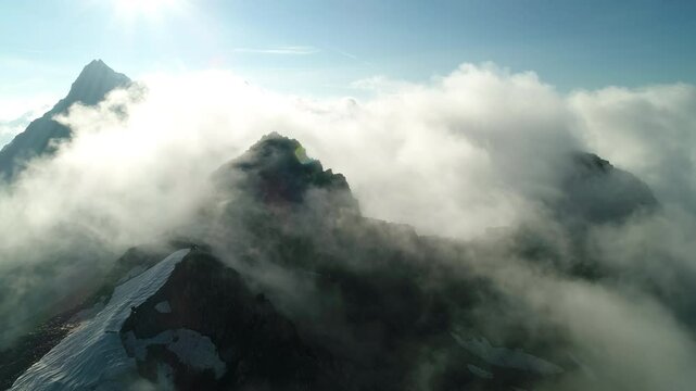 Aerial drone shot of heavenly mountain peak. Misty clouds traveling on top rugged rocky alpine cliffs. Dramatic alpine scenery summits.