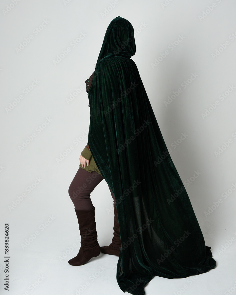 Canvas Prints Full length portrait of red haired female model, wearing green medieval fantasy costume, long flowing hooded velvet cape. Standing pose, walking away backwards , isolated white studio background.