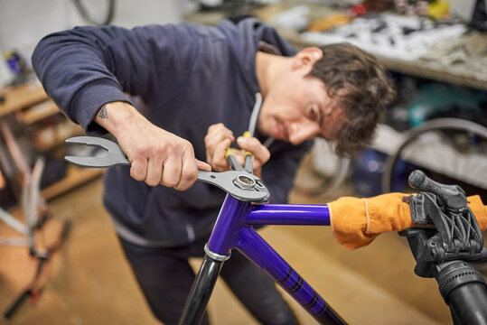 Young hispanic repairman assembling a bicycle in his bike workshop as part of a maintenance service. Real people at work.Composition with selective focus and copy space.