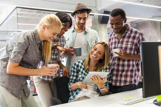 Diverse group of coworkers sharing a fun moment with coffee and tablet in modern office