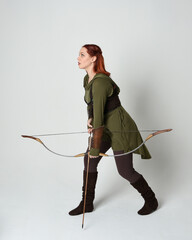 Full length portrait of red haired female model wearing green medieval fantasy costume, leather...