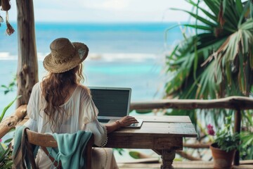 Fototapeta premium Woman in straw hat working on laptop at wooden table overlooking ocean beach travel and business concept
