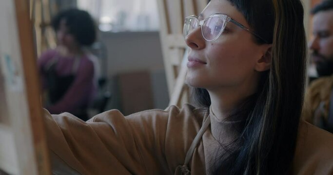 Young woman art student drawing with group of people focused on creative activity enjoying painting class in studio. Education and craftwork concept.