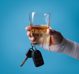 Adult Asian man with gauze bandage wrapped around his injured arms holding glass of alcoholic drink with car keys, closeup. Don't drink and drive concept