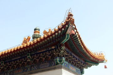 Fototapeta premium A photo of the top roof edge with traditional Chinese architecture, featuring ornate carvings and colorful patterns on its eaves, against a clear blue sky background. 
