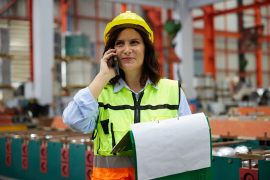 worker or engineer talking on smartphone and looking information on clipboard in the factory