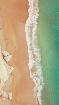 Vertical Screen: Enjoy a breathtaking aerial view of a sandy beach with turquoise waves gently kissing the shore, ideal for travel enthusiasts and nature lovers seeking tranquility and natural beauty