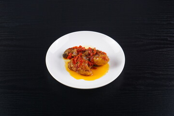 Indonesian typical balado fried chicken on a white plate on a black background with studio lighting