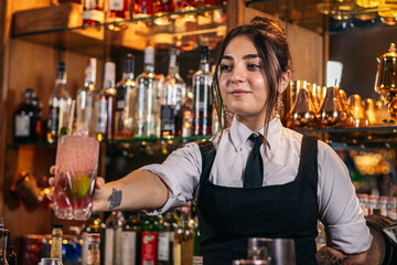 Young bartender offering a drink at the bar of a cocktail bar