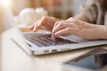 A close-up hand image of a woman working on her laptop computer, typing on the laptop keyboard.