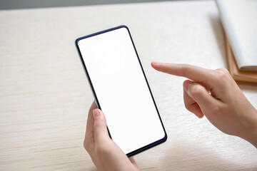 A close-up image of a woman sitting at a table indoors and using her smartphone.