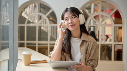 A woman is listening to music on her headphones and gazing the view outside of a cafe.