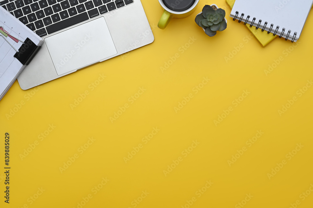 Wall mural Top view of laptop, notepad, coffee cup and financial documents on yellow background