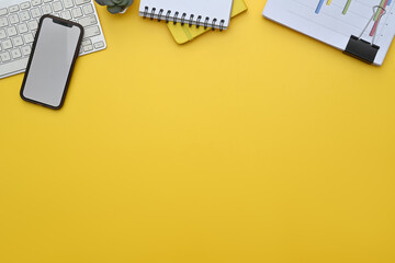 Smartphone, keyboard, notepad and financial documents on yellow background