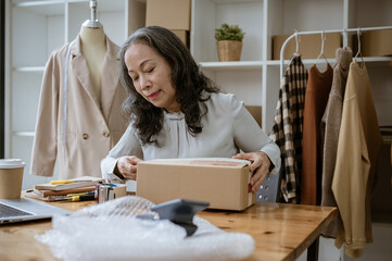 An experienced senior Asian female clothes online seller or tailor packing a cardboard box.