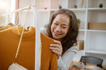 A mature female online clothing store owner is checking her new products on a rack in her studio.