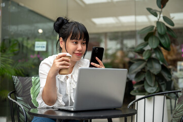 A woman is working remotely from a cafe in the city, sipping coffee, and using her smartphone.