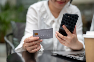 A young Asian woman holding a credit card and her smartphone while sitting at a table outdoors.