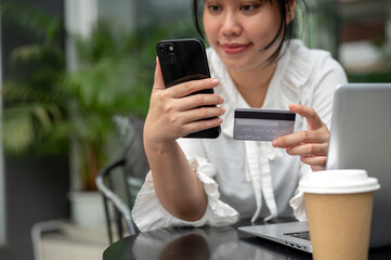A young Asian woman holding a credit card and her smartphone while sitting at a table outdoors.