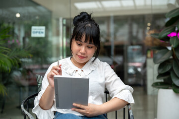A young Asian woman reading something on her digital tablet, working remotely from a coffee shop.