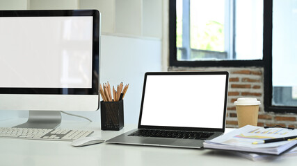 Fototapeta premium Blank computer monitor, laptop and financial document on white table in office