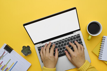 Above view unrecognizable woman hands typing on laptop keyboard over yellow background