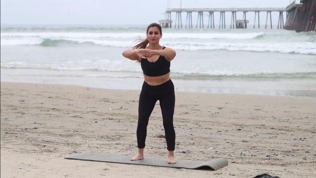 mature latina woman training doing squats on the beach next to pier, mexican