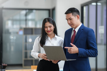 Professional colleagues discussing work on a laptop in a modern office setting. Business attire signifies a formal work environment.