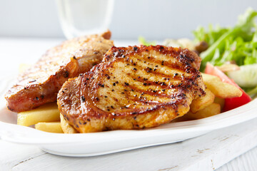 Grilled Steaks with french fries and fresh salad. Bright wooden background.