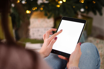 Mock-up, tablet in the hands of a woman. Christmas tree background. Concept of online shopping, discounts 