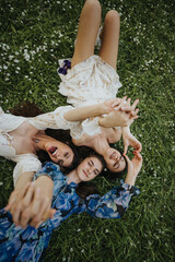 Fototapeta premium This compelling image captures three young girls in floral dresses enjoying a blissful moment lying on the grass, surrounded by small flowers in a park.