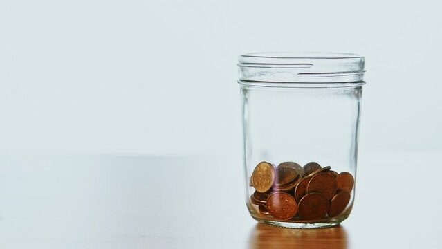 Slow motion video of many coins falling into the jar