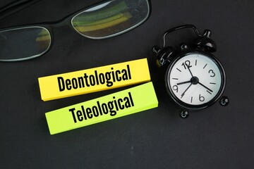 glasses, bell clock and colored paper with the words two systems of ethics ie Deontological and...