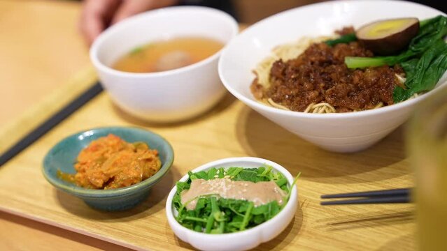 Chopsticks eating dry pork ramen with green vegetable and spiced corned egg fusion Chinese Japanese noodle with side dishes