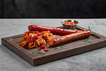 German sausages (bratwurst), traditional sausage dish of German cuisine, on a wooden board, next to stewed cabbage and bowl of red sauce. spicy and smoked meat delicacies prepared on the grill.