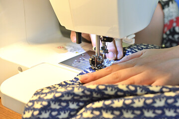 ミシンを操作する手。手で布を送っている。