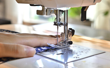 ミシンを操作する手。手で布を送っている。