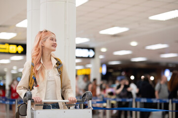 Young traveler with luggage cart and backpack at airport terminal. Concept of travel, exploration, and excitement