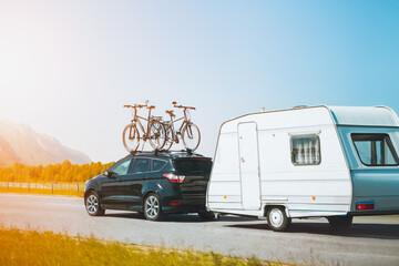 Car with bicycles mounted on top towing a caravan on a sunny highway against a scenic mountain...