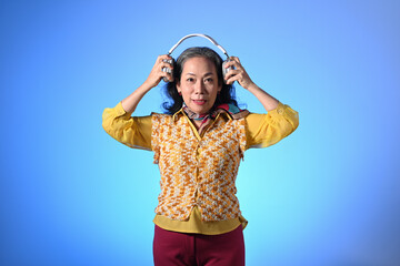 Portrait of beautiful elderly woman wearing headphone standing against light blue background